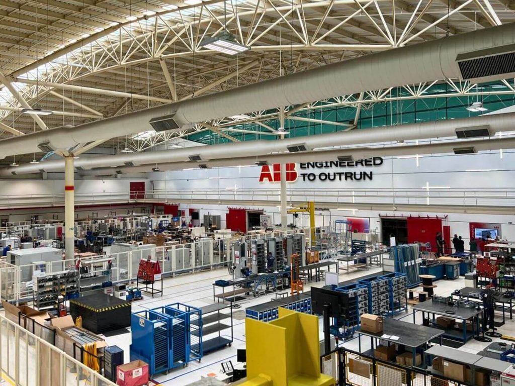Oficina principal da ABB Robotics em Sorocaba, com braços robóticos laranja em bancadas de montagem e teste