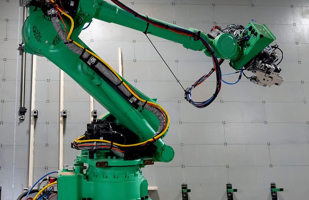Braço robótico industrial verde numa microfábrica da Reframe, com cabos presos ao longo do braço e a ferramenta na ponta